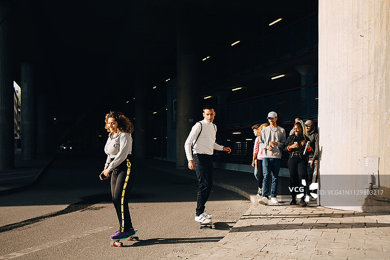 朋友们观看晴天时在路上玩滑板的男女图片素材