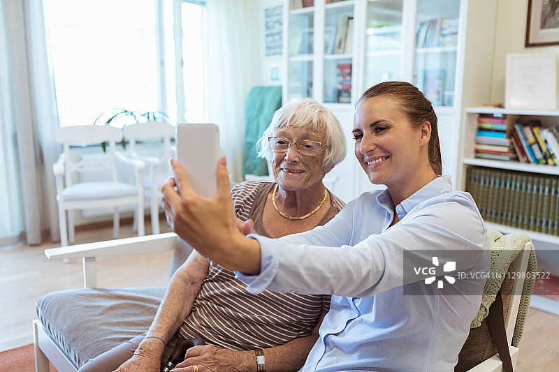 在疗养院探访期间，微笑的年长女性和孙女用手机自拍图片素材