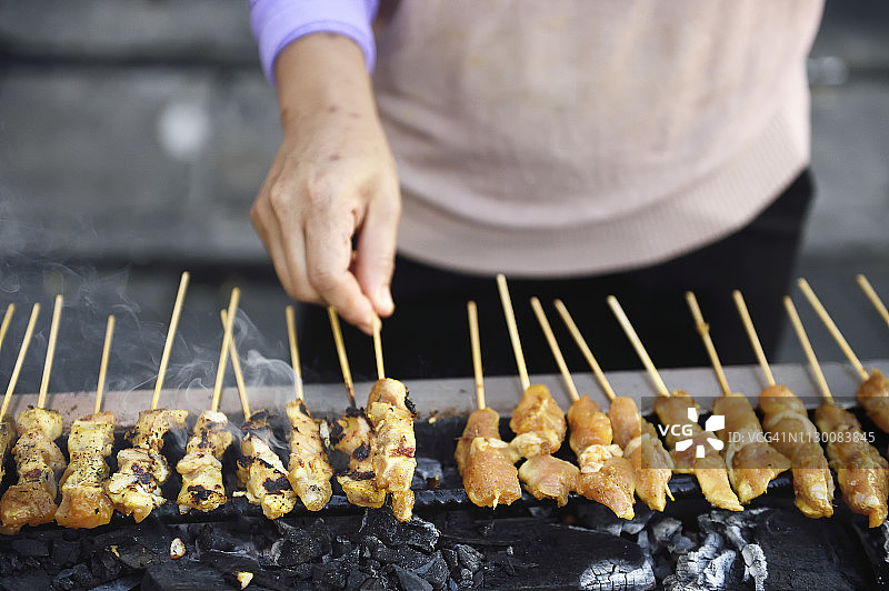 手在炭火烤架上翻动沙爹肉串图片素材