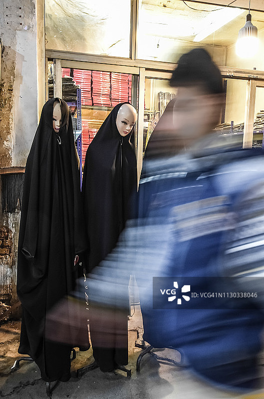 伊朗伊斯法罕巴扎，两个穿着传统宗教头巾的人体模型，前方一个模糊的人影经过图片素材