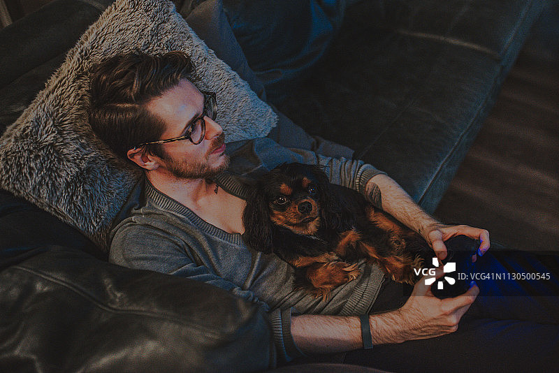 年轻男人抱着查理王小猎犬在家玩电子游戏图片素材