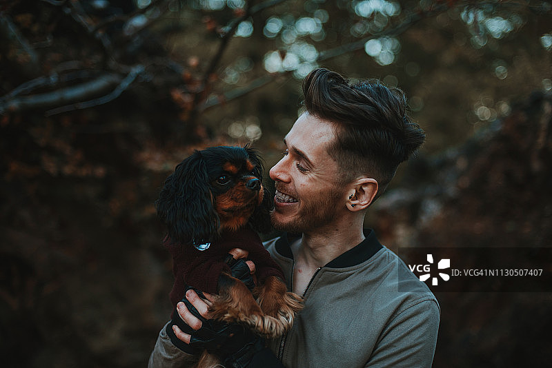 年轻微笑的男子抱着一只查理王小猎犬图片素材