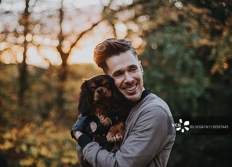 年轻微笑的男子抱着一只查理王小猎犬图片素材