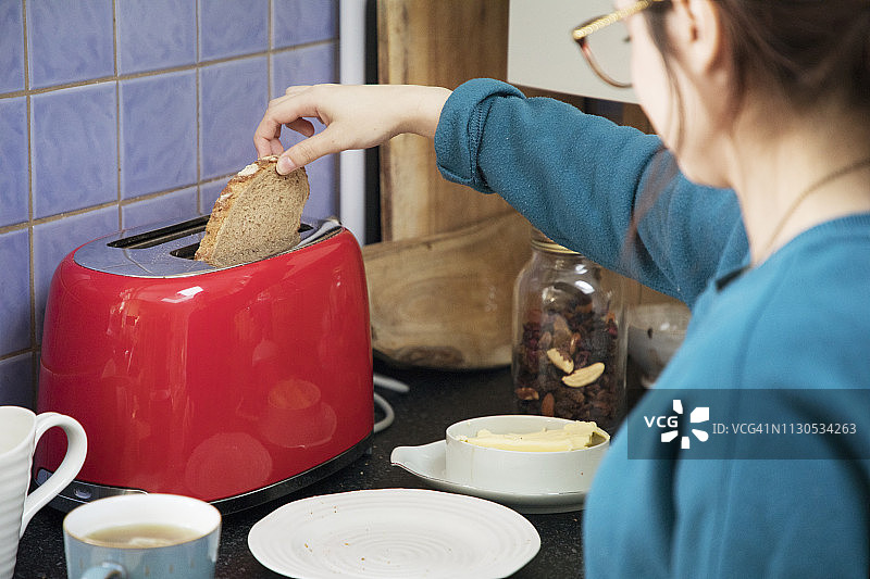 女人从烤面包机中取出吐司，过肩视角图片素材