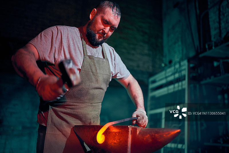 强壮的络腮胡铁匠锻造通红的金属棒图片素材