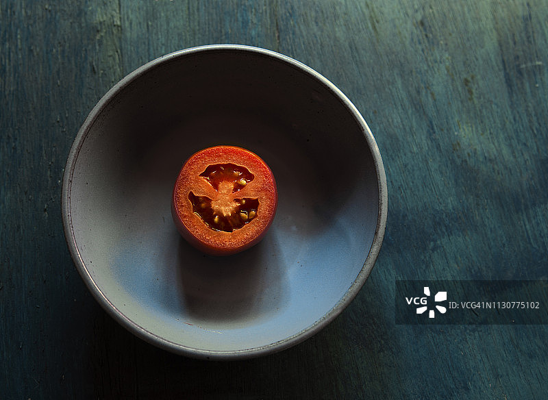 蓝色背景下的蓝色碗中半个番茄静物图片素材