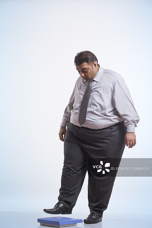 穿着正装踩在体重秤上的肥胖男子图片素材