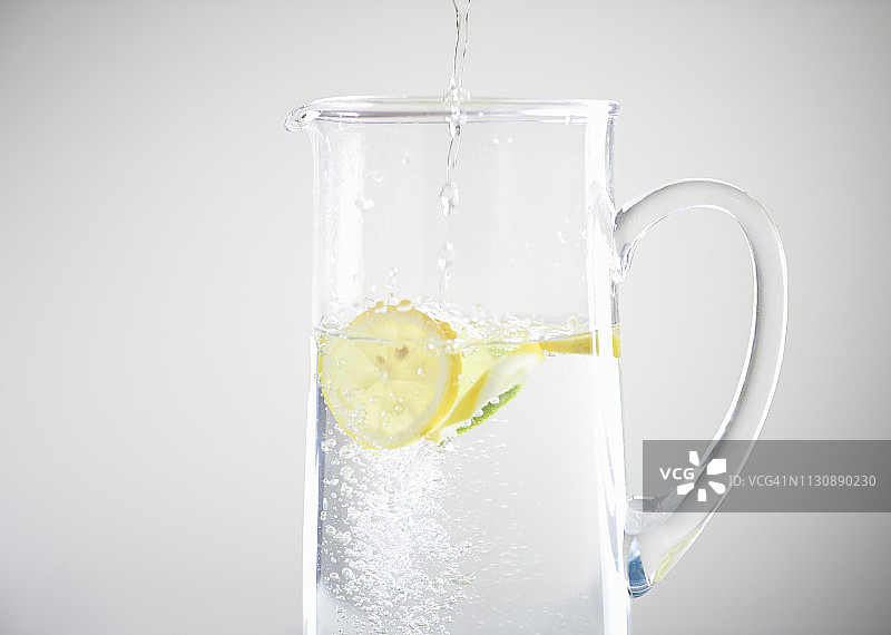 将水倒入装有新鲜柠檬和酸橙的玻璃水罐中图片素材