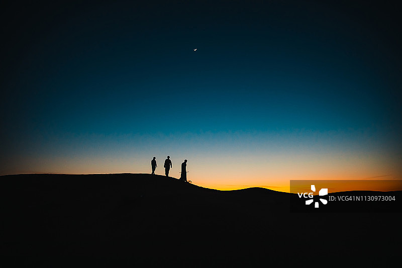 黄昏时分在沙丘上行走的阿拉伯人图片素材