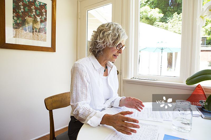 在桌边看文件并用手势表达的中年妇女图片素材