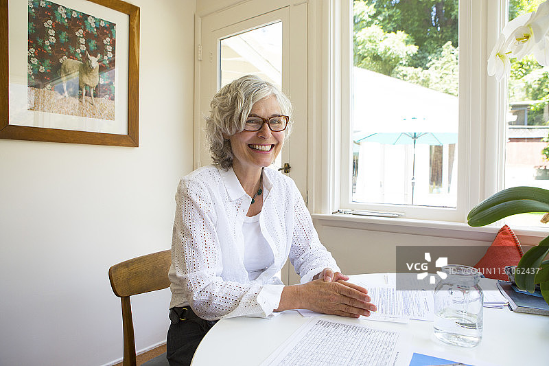 坐在白色桌子旁，对着镜头灿烂微笑的50年代白发女人图片素材