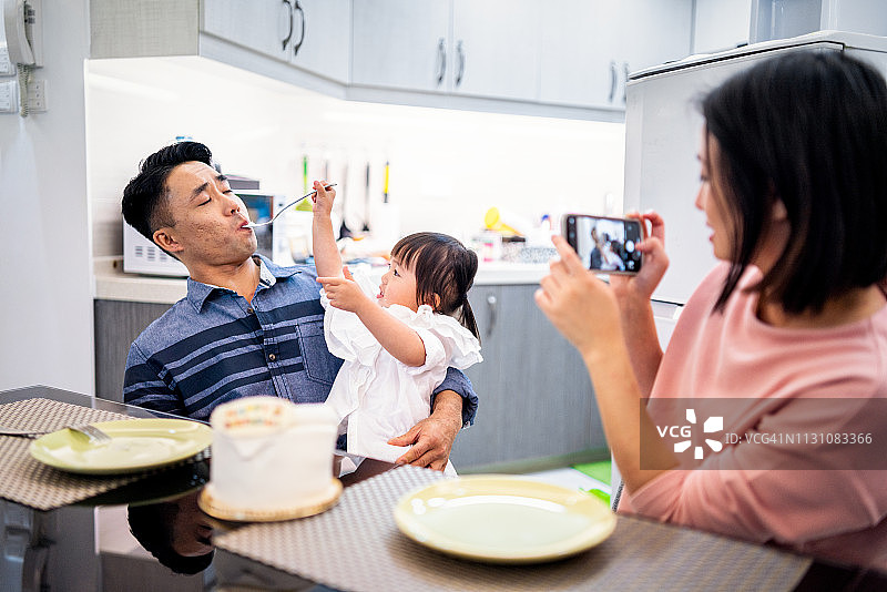 母亲拍摄可爱的小女孩喂爸爸图片素材