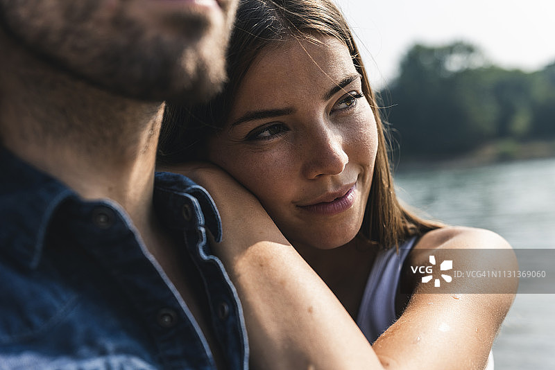 微笑的年轻女子靠在河边男人的肩膀上图片素材