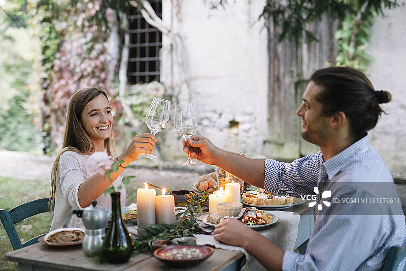 情侣在小屋旁享用浪漫的烛光晚餐，碰着葡萄酒杯图片素材