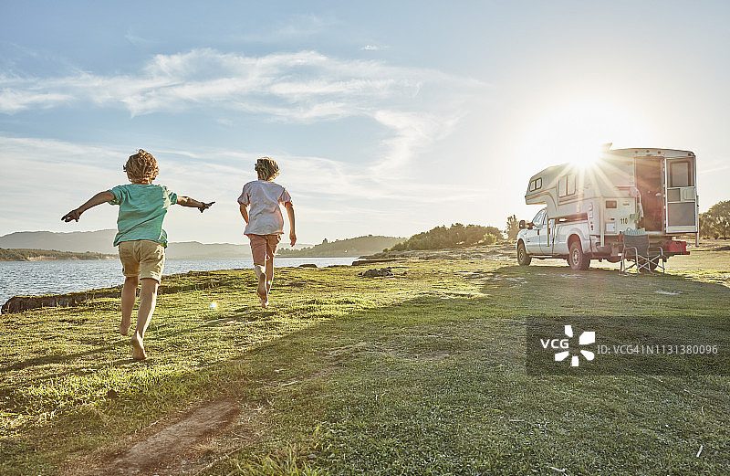 智利塔尔卡：在马乌莱河畔，两个男孩在露营车旁的草地上奔跑图片素材