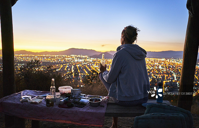 智利圣地亚哥，日落时分，女人在城市上方的山中喝啤酒图片素材