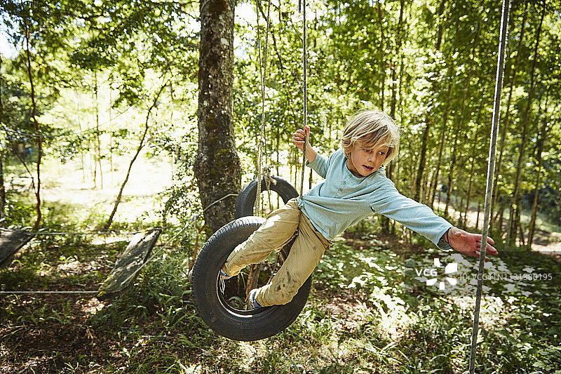 男孩在森林探险公园的轮胎上保持平衡图片素材