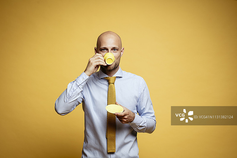 光头商人喝咖啡的肖像（黄色背景）图片素材