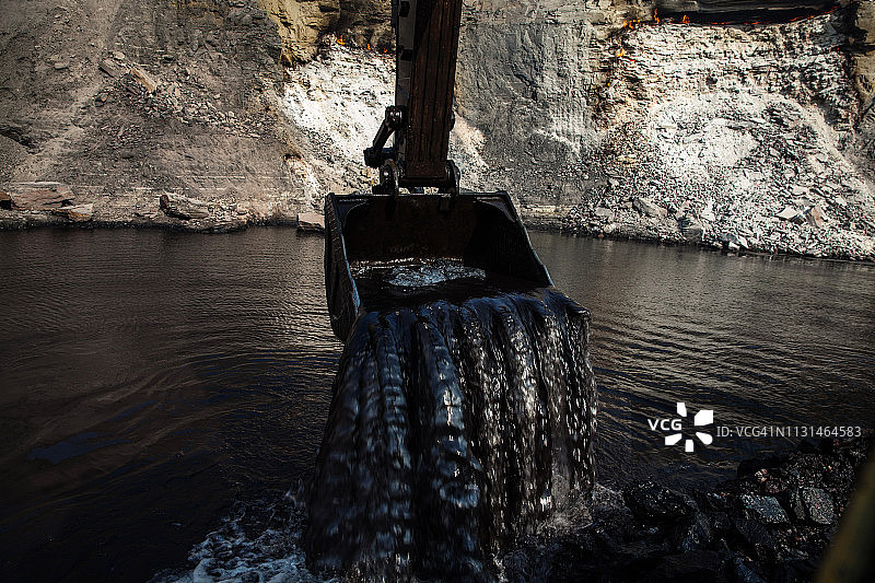 挖掘机铲斗倾泻水流，煤矿在水面下开采图片素材