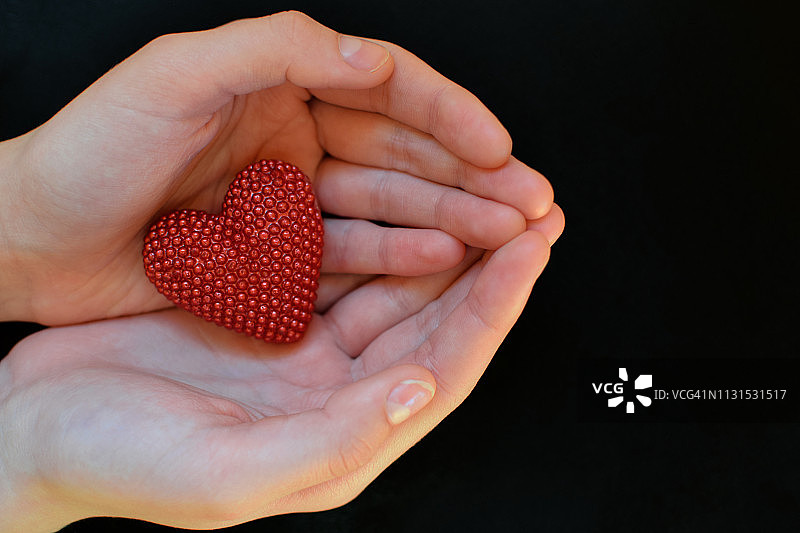 黑色背景下人手中的红色爱心图片素材