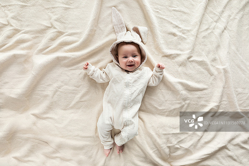 可爱的宝宝穿着兔子服装躺在家里的毯子上，俯视图图片素材