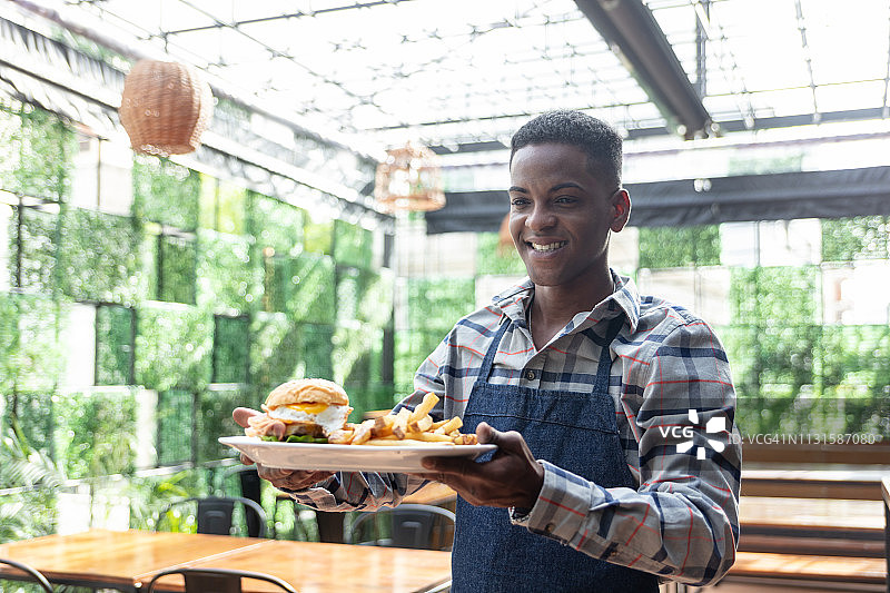 友善的黑人男服务员在餐厅为顾客点汉堡和薯条图片素材