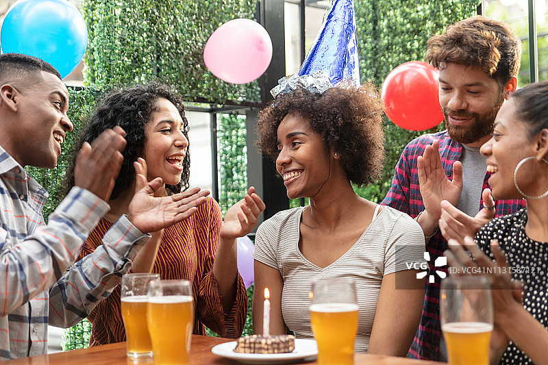 戴着生日帽，朋友们唱歌时面带微笑的漂亮黑人女人图片素材