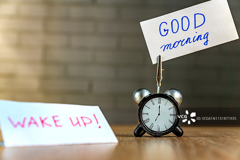 木桌上的闹钟和手写“早安”横幅，时间管理概念图片素材