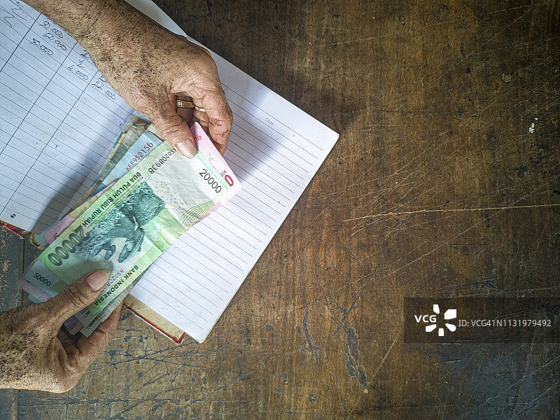 老商业女性在经典木桌上方拿着印尼盾纸币和商业手册。一个商业和金融概念。图片素材