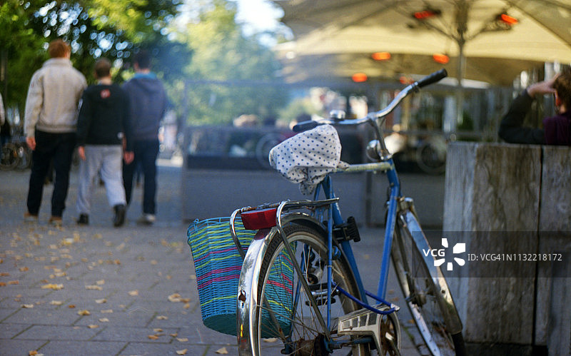 蓝色自行车停在人行道咖啡馆旁，配有蓝色车篮和圆点座套图片素材