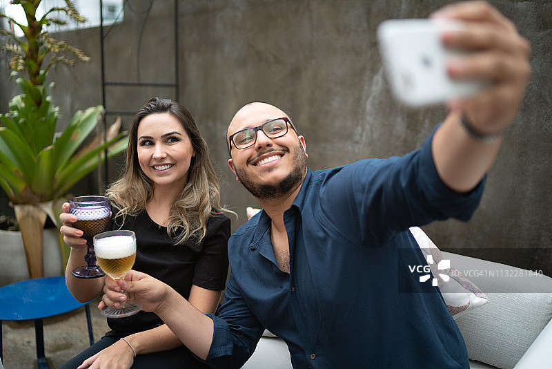 情侣在沙发上一起喝酒，男人拿着智能手机自拍图片素材