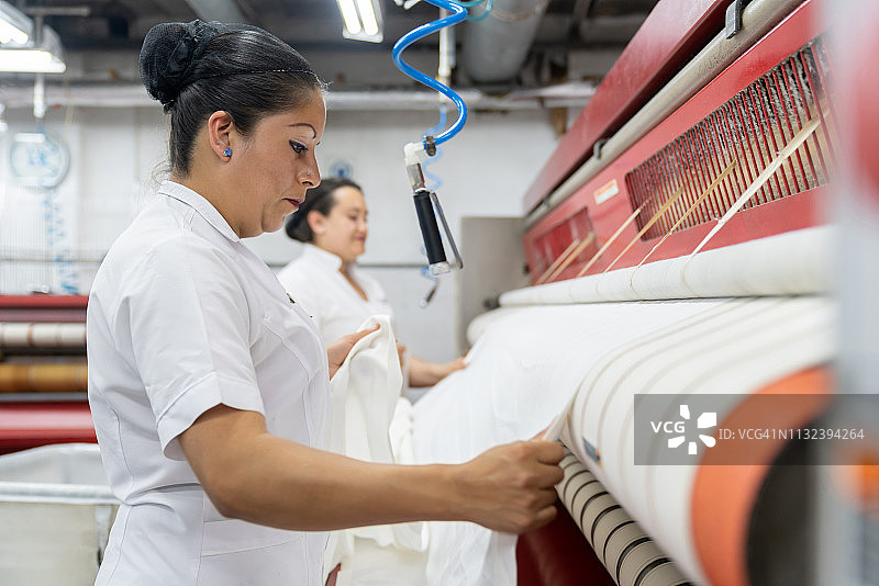 拉丁美洲女性用工业熨斗熨烫床单图片素材