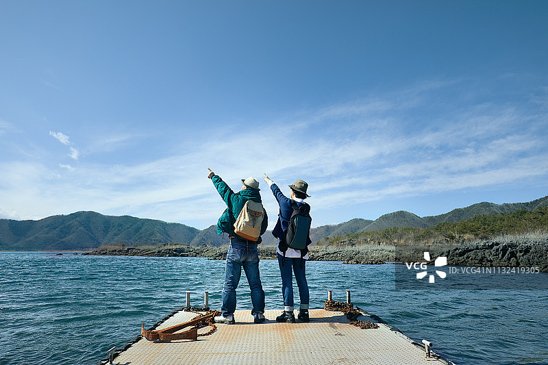 带着背包站在阳光下湖泊码头上的男人和女人。年长的男人和女人来到日本本栖湖观光图片素材