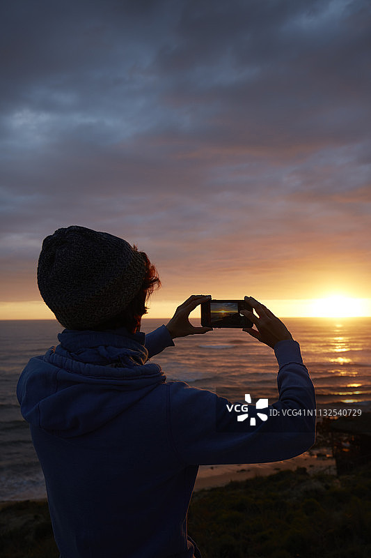 日落时在海滩上拍照的女人图片素材