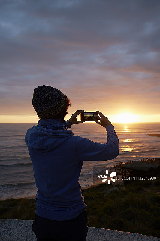 日落时在海滩上拍照的女人图片素材