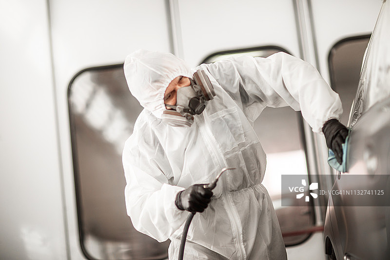 汽车维修技师在喷漆室内为汽车的四分之一面板涂上一层透明涂层图片素材