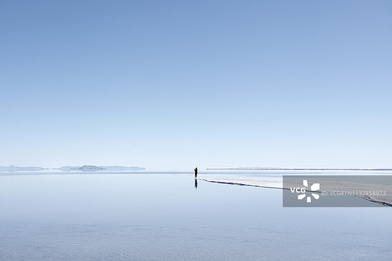 游客在盐湖城外拍摄盐滩和静水倒影，晴空万里图片素材