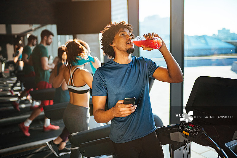 年轻男人在跑步机上锻炼时喝提神饮料图片素材