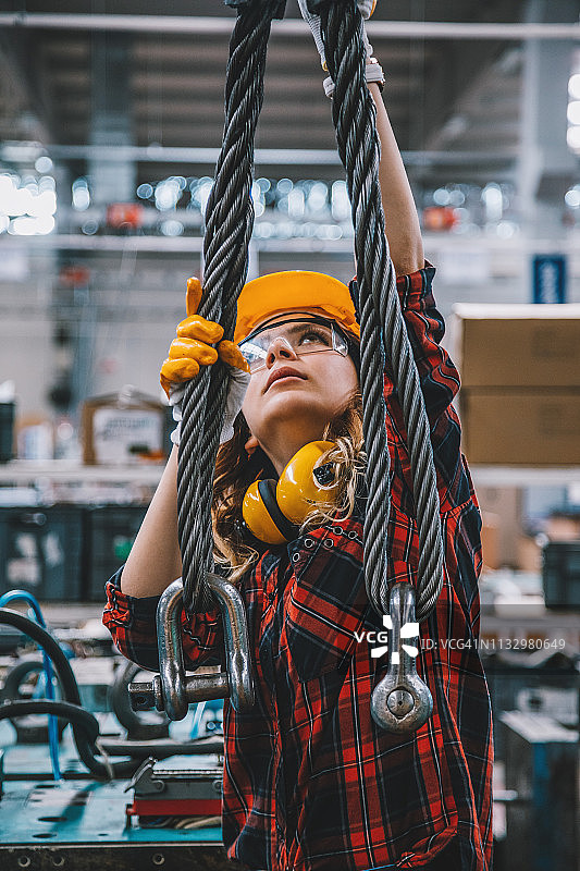 在工厂里用起重机吊钩工作的重工业女工图片素材