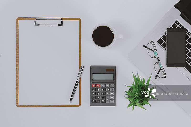 办公桌上的空白白纸剪贴板、计算器和笔记本电脑图片素材