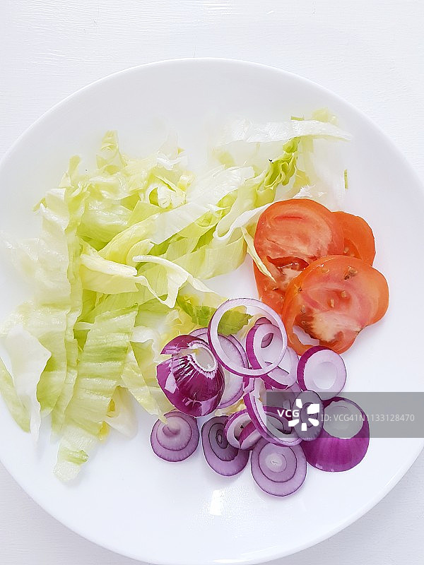 白盘上新鲜切好的生菜、番茄和红洋葱图片素材