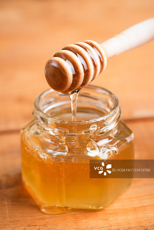 罐子里流淌的蜂蜜和木制蜂蜜勺图片素材