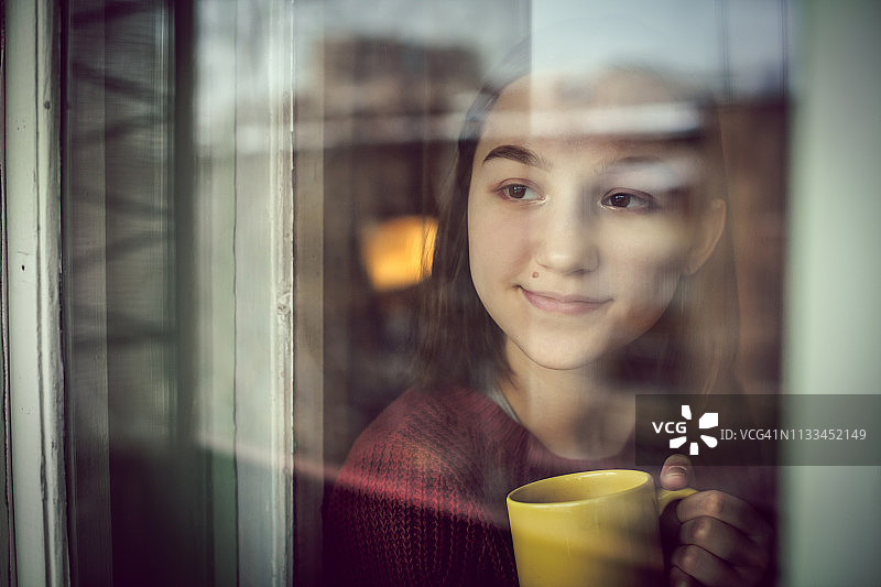 喝着茶或咖啡、望着窗外的快乐女孩图片素材