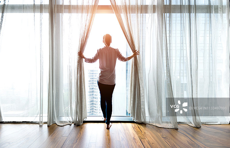女人拉开窗帘向外看图片素材