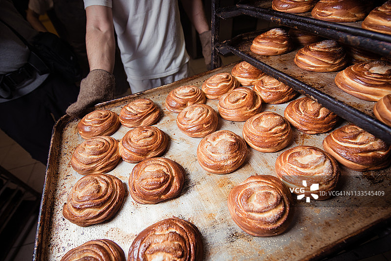 戴着手套的面包师拿着装有甜面包的烤盘图片素材
