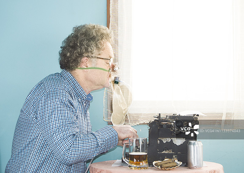 一个用旧打字机工作的人，抽着雪茄，戴着氧气面罩图片素材