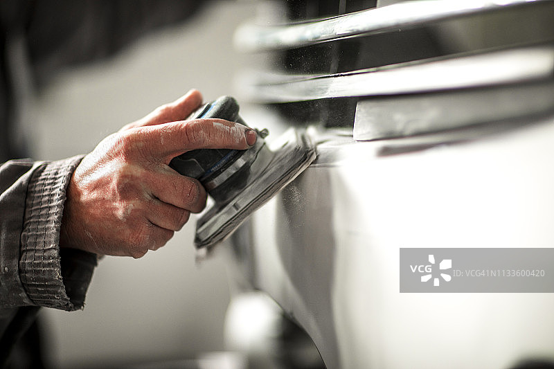 使用便携式电动砂光机打磨汽车翼子板上的填充物图片素材