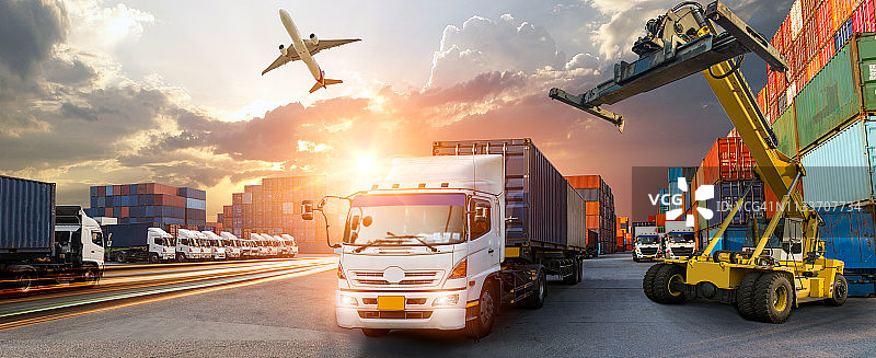 集装箱卡车在港口进行商业物流和运输，日出时船坞内有集装箱货轮和货机以及起重机桥，物流进出口和运输行业背景图片素材