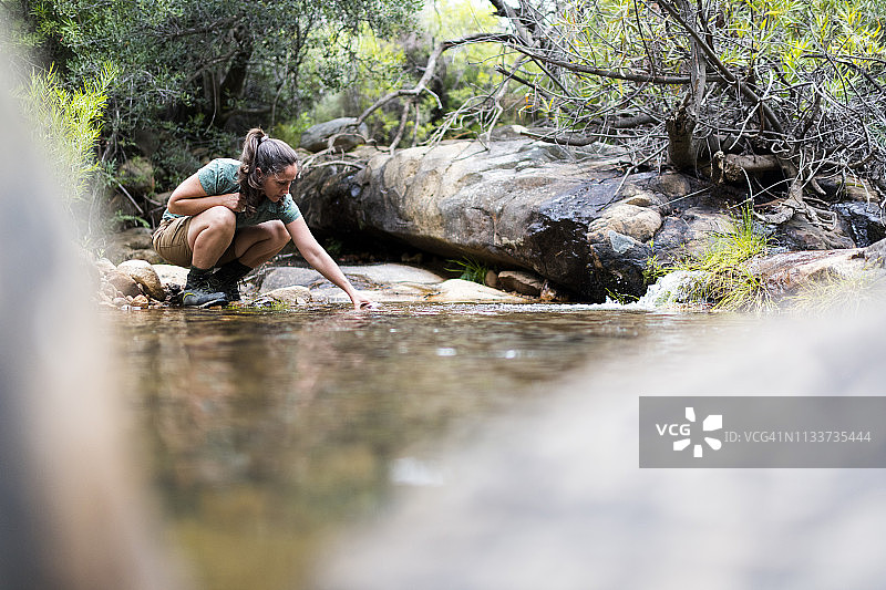 一位女士从流动的溪流中舀水到她的水瓶里图片素材