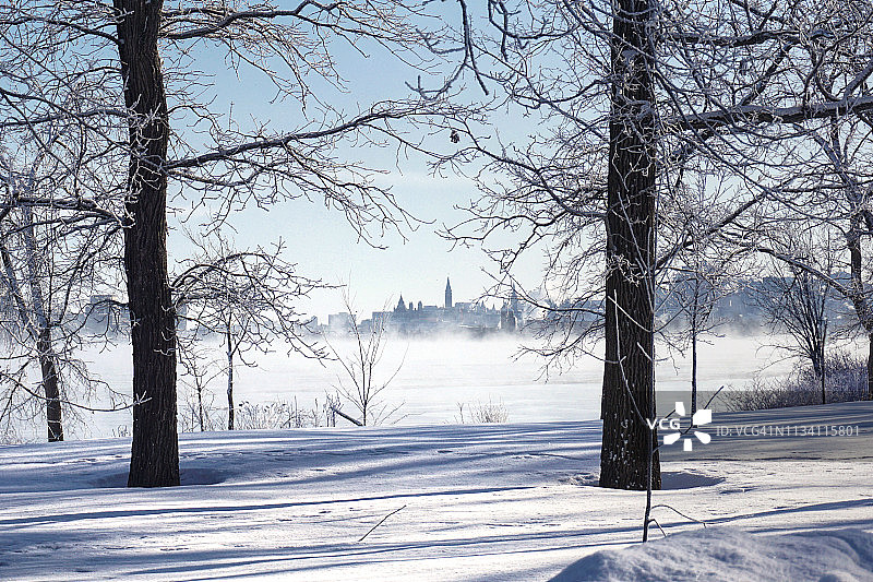 从被白雪覆盖的贝特岛看到的加拿大议会冬季景色，渥太华河上升起薄雾图片素材